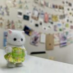 会社に貼り出している制作物をバックに微笑むシルバニア